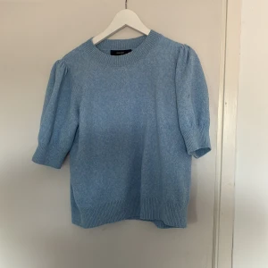 Ljusblå stickad tröja från Vero Moda - Säljer en ljusblå stickad tröja från Vero Moda med puffärmar och ribbade muddar vid hals, ärmslut och nederkant. Tröjan har en rund halsringning och trekvartsärm, perfekt för lager-på-lager-stil.