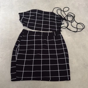 Svart och vit rutig croppad topp - Säljer en svart croppad topp med vitt rutmönster och smala knytband. Toppen är ärmlös och har en modern, trendig look som passar perfekt till kjol eller jeans.