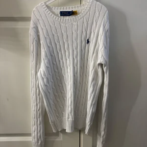 Vit kabelstickad tröja från Polo Ralph Lauren - Vit kabelstickad tröja från Polo Ralph Lauren med rund halsringning och diskret broderad mörkblå logga på bröstet. Den är endast använd 1-2 gånger så nästan i nyskick. Den är i dammodell och är köpt i USA på Polo Ralph Lauren. Säljer då den inte är min stil längre💕