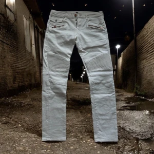 True religion Biker Jeans  - Biker jeans från True religion i vit färg. Jeansen är i grymt skick förutom en väldigt lättsam defekt som syns på sista bilden. Sjukt feta par jeans Påmminer om Balmain Biker jeansen. De har en slim fit. Person på bild är 187cm och 73kg men referera till måtten: Midja 42.5 inseam 73cm rise 30 cm total längd 100,5cm sida till sida av slutet av jeansen 17cm.