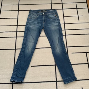 Blå Replay jeansbyxor herr w29 - Säljer ett par klassiska blå jeans från Replay i modellen w29. Jeansen har normal passform, raka ben och snygga slitningar framtill. Flera fickor och Replay-logga på fickan. Perfekta för dig som gillar stilrena och bekväma jeans.