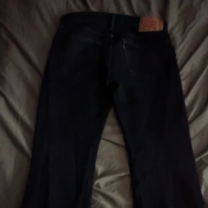 Mörkblå Levis 501 jeans - Säljer ett par klassiska svarta Levis 501 jeans med raka ben och femficksdesign. Byxorna har den ikoniska Levis-lappen bak i midjan och röd Levis-tagg på bakfickan. Perfekta för dig som gillar tidlös denimstil.