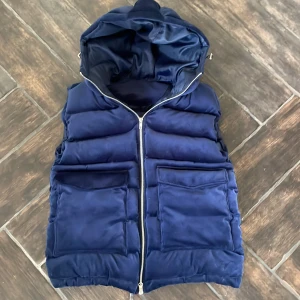 Blå dunväst från vendiera - Snygg blå dunväst från vendiera med dragkedja och huva. Västen har två stora fickor framtill och är perfekt för kyligare dagar. Den har en stilren design med ett diskret märke på fickan. Knappt andvänd. Västen är mycket eftertraktad och är slutsåld på vendieras hemsida.