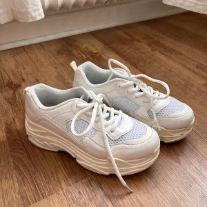 Chunky vita sneakers med meshdetaljer från Duffy - Säljer ett par chunky vita sneakers från Duffy med meshdetaljer och snörning. Skorna har en tjock plattformssula och rund tå, vilket ger en sportig och trendig look. Perfekta för dig som gillar streetstyle och vill ha bekväma skor till vardags.