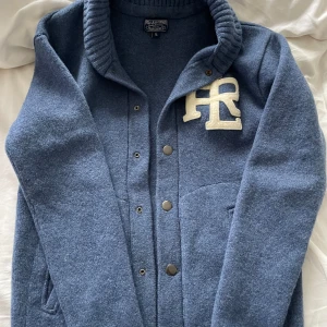 Polo Ralph Lauren kofta - Säljer en snygg blå kofta/cardigan från Polo Ralph lauren med knappar och en broderad logga på bröstet. Koftan har en hög krage och ribbade muddar som ger en stilren look. Storlek M, men sitter snarare som S. 