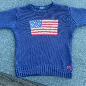 Blå stickad Ralph lauren tröja  - Säljer en blå stickad tröja från Polo Ralph Lauren i barnstorlek L, Vilker motsvarar XS. Tröjan har ett broderat USA-flagga-motiv på bröstet och RL-broderi nertill. Tillverkad i 100% bomull och har ribbade muddar vid ärmslut och nederkant. Bra skick , pris går att diskutera 