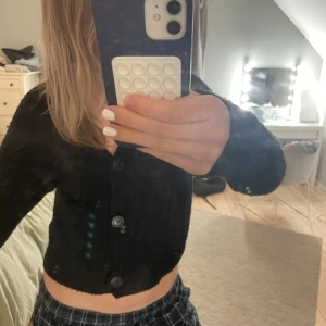 Svart ribbad kofta från Kappahl  - Säljer en svart ribbad kofta från Kappahl. Koftan är croppad med v-ringning och har tre knappar framtill. Perfekt att styla med både jeans och kjol. Materialet är mjukt och stretchigt.