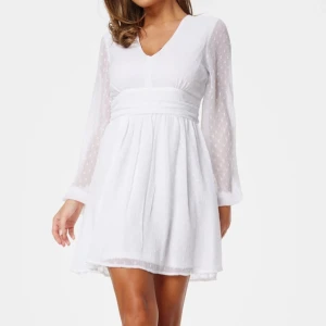 Studentklänning - Superfin studentklänning med v-ringad hals, långa transparenta ärmar och markerad midja med knytband bak. Prickigt mönster i tyget och lätt volang i kjolen. Bara använd en gång! Nypris 599kr 