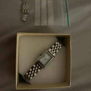 Silverfärgad rektangulär damklocka - Silver klocka från mockberg. Extra länkar medföljer för justering av storlek. Nackdelar är att batteriet i klockan är dött.