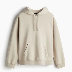Beige hoodie från H&M - Säljer en stilren beige hoodie från H&M med klassisk huva. Tröjan har en stor magficka och ribbade muddar vid ärmslut och nederkant. Perfekt för en avslappnad och enkel look. 