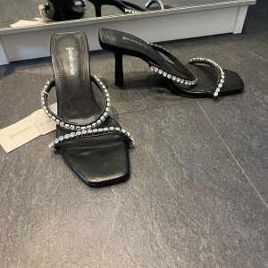 Svarta klackade sandaler med strass från Stradivarius - Snygga svarta sandaler med klack från Stradivarius. Skorna har två remmar dekorerade med glittrande strass och fyrkantig tå. Perfekta för att lyfta din outfit med lite extra bling.
