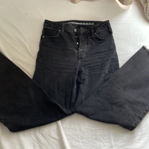 Svarta wide leg jeans - Säljer ett par svarta jeans med hög midja och raka, vida ben. Byxorna har klassisk femficksdesign och knäppning med knappar framtill. Perfekta för en avslappnad och trendig stil.