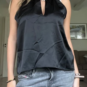 Svart satinlinne - Snygg svart ärmlös topp i satin med pärldetalj vid halsen och en liten v-ringning framtill. Toppen har en lös passform och är perfekt att styla med jeans eller kjol!!💕 Toppen är aldrig använd, så den är i toppenskick! Endast 150 kr!