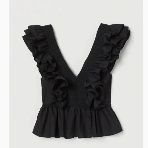 Svart volangtopp med v-ringning💕 - Säljer en svart topp med djup v-ringning och stora volanger längs axlarna. Toppen har en croppad passform och smockdetaljer framtill. Perfekt för att lyfta en outfit med lite extra volym och stil.