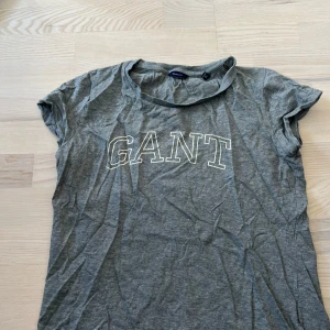 Grå t-shirt från GANT - Säljer en grå t-shirt från GANT med vit logotyp tryckt framtill. T-shirten har korta ärmar och en klassisk rund halsringning. Perfekt basplagg till garderoben!
