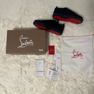 Mörkblå sneakers från Christian Louboutin - Säljer ett par mörkblå sneakers från Christian Louboutin med klassisk röd sula och rund tå. Skorna har snörning och är tillverkade i mocka med detaljer i skinn. Kommer med originalkartong och dustbag.