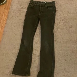 Svarta bootcut jeans från gina - Säljer ett par grå/svarta bootcut jeans med klassisk femficksdesign och dragkedja. Jeansen har en lätt utsvängd passform nertill och är tillverkade i ett stretchigt denimtyg. Perfekta för dig som gillar en tidlös look. Lite sliten på vissa ställen men knappast så man märker och helt sliten på lappen. 