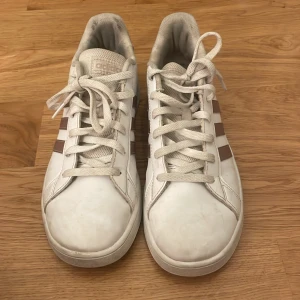 Vita Adidas sneakers med bruna ränder - Säljer ett par klassiska vita Adidas sneakers med ränder på sidorna och vit sula. Säljer då ja tröttnat på de. 