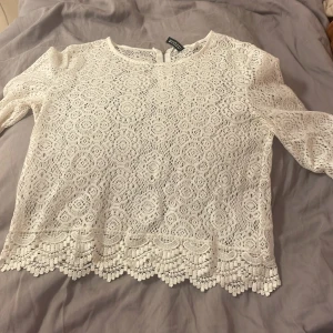 Vit spetsblus med trekvartsärm - Säljer en söt vit spetsblus från Bik Bok med vackert virkat mönster och dekorativ kant nertill. Blusen har trekvartsärmar och rund halsringning. Perfekt att styla till jeans eller kjol!