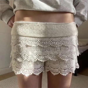 Spets shorts - Superfina vita shorts med virkad spets och vågig kant. De har bred resår i midjan och ett romantiskt, boho-inspirerat utseende. Perfekta för varma dagar när du vill ha något både bekvämt och snyggt.