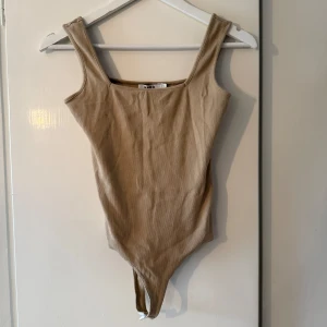 Body från Nakd - Säljer ett beige bodycon-linne från NA-KD med fyrkantig urringning och öppen rygg. Sitter tight och framhäver figuren på ett snyggt sätt – perfekt att styla upp eller ner beroende på tillfälle.  Använt ett fåtal gånger och i fint skick. Pris kan diskuteras. Skriv gärna för fler bilder!🌸