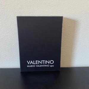 Svart Plånbok från Valentino - Snygg svart Plånbok från Valentino med flera kortfack och stilren logga framtill. Perfekt för att hålla ordning på dina kort i en smidig och kompakt design. Levereras i originalförpackning.
