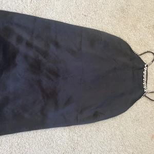 Svart halternecktooo med pärldetaljer från H&M - Svart halternecktooo med pärldetaljer från H&M. Säljer en svart halternecktopp från H&M med tunna axelband och pärldetaljer längs urringningen. Klänningen har en elegant och enkel design, perfekt för speciella tillfällen. Ej andvänd men saknas ”pärlor” på banden