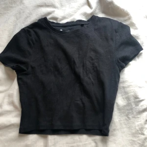 Svart  croppad t-shirt  - Säljer en svart croppad t-shirt. T-shirten är ribbad och har korta ärmar samt rund halsringning. 