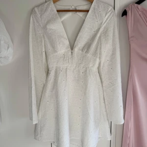 Studentklänning  - Vit kortklänning med broderade detaljer och v-ringning. Öppen i ryggen och passar perfekt till studenten. 
