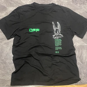 Svart t-shirt med tryck från Off-White - Svart t-shirt från Off-White med grönt och vitt tryck framtill och baktill. Framtill finns en tecknad kanin, text om 'The Golden Ratio' och logga. Baktill stort tryck med kanin och text. Skön och trendig modell.