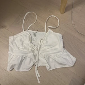 Vit croppad linnetopp med knyt - Säljer en söt vit croppad linnetopp med tunna axelband och knyt framtill. Perfekt för varma dagar och enkel att matcha med jeans eller kjol.