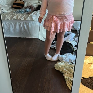 Rosa omlottkjol med volang - Supersöt rosa kortkjol med vitt mönster och volangkant. Kjolen har omlottmodell med knyt i sidan och är perfekt för en trendig look. Lätt och luftig känsla, passar perfekt till varmare dagar.