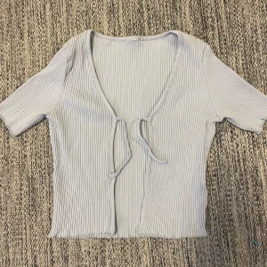 Ljusblå ribbad topp som knyts  - Säljer en ljusblå ribbad topp med korta ärmar och knyt framtill. Toppen har en croppad passform och är snyggt att ha över något men även bara som den är 😊