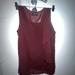 Vinröd ärmlös blus från Vila - Säljer en vinröd ärmlös blus från Vila med snygga lager på framsidan som ger en stilren look. Perfekt att matcha med jeans eller kjol för en trendig outfit. 