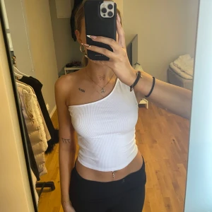 Vit ribbad oneshoulder topp från Gina Tricot - Säljer en vit ribbad oneshoulder topp från Gina Tricot. Toppen är croppad och har en tight passform med en axelbandslös design på ena sidan. Perfekt för sommaren och enkel att matcha med olika outfits.