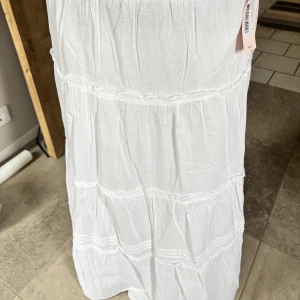 Vit långkjol med volanger - Luftig, lång och superfin somrig kjol som är helt oanvänd och tyvärr inte heller kommer komma till användning då jag har en likanande. Pris kan diskuteras vid snabb affär!