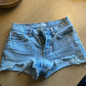 Ljusblå jeansshorts från MNG - Säljer ett par ljusblå jeansshorts från MNG, modell Hailey. Shortsen har fransiga benslut, knappar i gylfen och klassisk femficksdesign. Perfekta för varma dagar och enkel att matcha med olika toppar. Väldigt bra skick, men använd många gånger. Säljer pågrund av att jag har växt ur dem tyvärr.