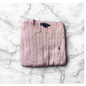 Rosa stickad Ralph Lauren tröja - Säljer en rosa tröja från Ralph Lauren i storlek Large (L), dammodell. Tillverkad i 100% bomull och pryds av den klassiska svarta broderade loggan på bröstet. Tröjan är mjuk och skön – perfekt till både vardag och avslappnade tillfällen.  🔹 Detaljer: ✔ Färg: Rosa ✔ Storlek: L (Large) ✔ Modell: Dam ✔ Material: 100% bomull ✔ Logga: Svart Ralph Lauren-logga ✔ Skick: Använd – lite urtvättad vid kragen och viss färgförändring upptill, annars i bra skick.