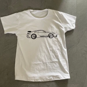 Limiterad Porsche T-shirt - Säljer en vit t-shirt med ett stilrent svart tryck av en porche på bröstet. T-shirten har rund halsringning och korta ärmar. Hör av dig om du har några funderingar⭐️