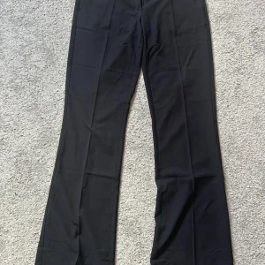 Svarta kostymbyxor från Nelly - Säljer ett par svarta kostymbyxor från Nelly med klassisk passform och raka ben. Endast använda 2 ggr då jag upplever de för stora på mig som är storlek 32 egentligen. Byxorna har låg midja och är tillverkade i ett mjukt material som ger en snygg siluett. Perfekta att styla med sneakers eller klackar.