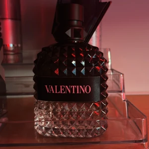 Valentino parfymflaska med nitar - Säljer en lyxig parfym från Valentino i en genomskinlig glasflaska med nitar och svart etikett. Flaskan har en unik, diamantmönstrad design och svart kork. Perfekt för dig som gillar exklusiva dofter och snygg inredningsdetalj.