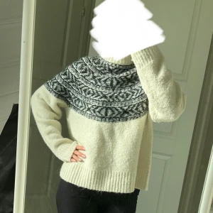 Vit stickad tröja - Säljer en vit stickad tröja med svart och grått mönster över axlarna. Tröjan har lång ärm och en rak, lite loose passform. Perfekt för kyliga sommarkvällar och riktigt mysig att bära. Använt 1 gång.