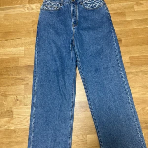 Blå jeansbyxor från Coach med mönstrade fickor - Säljer ett par blå jeansbyxor från Coach med unika fickor i blått mönster. Byxorna är baggy med klassisk femficksdesign. Perfekta för dig som vill ha något som sticker ut lite extra. Aldrig använda
