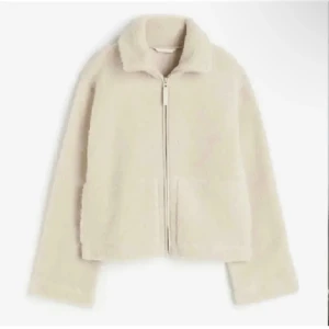 Beige teddyjacka med dragkedja - Mysig beige teddyjacka med hög krage och dragkedja framtill. Jackan har två fickor och är perfekt för kyligare dagar. Passar till jeans och t-shirt för en avslappnad look.