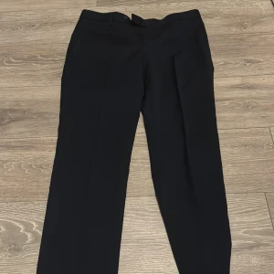 Mörkblåa kostymbyxor med klassisk passform - Snygga mörkblå kostymbyxor med normal passform och raka ben. Byxorna har diskreta fickor fram och bak, samt hällor för bälte. Perfekta till en dressad look och tillverkade i ett slätt material som känns bekvämt.