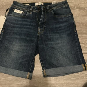 Mörkblå jeansshorts från Selected - Snygga mörkblå jeansshorts från Selected med klassisk femficksdesign och uppvikta benslut. Shortsen har normal passform och är tillverkade i stretchigt denim för extra komfort. Perfekta för varma dagar och enkel att matcha med t-shirt eller skjorta.