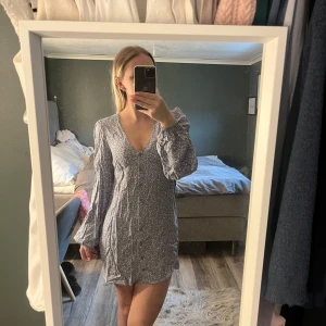 Blommig kortklänning med v-ringning - Söt kortklänning med ljusblå botten och små vita blommor. Klänningen har v-ringning, långa och pösiga ärmar. Perfekt för vår och sommar!