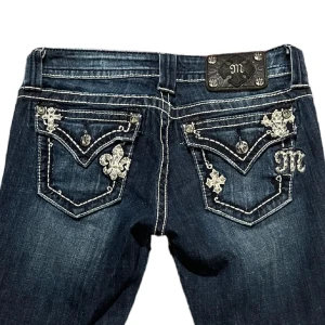 Mörkblå bootcut jeans med broderade detaljer - Säljer ett par mörkblå jeans med bootcut passform och snygga broderade detaljer på bakfickorna. Två hål mellan benen som täcks av jeanstyg inne ifrån men går att sprätta upp och sy igen❤️syns ej när jag promenerar normalt