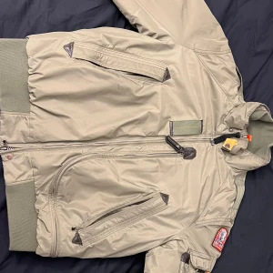 Grön bomberjacka från Parajumpers - Säljer en grön bomberjacka från Parajumpers med orange quiltat foder. Jackan har dragkedja, flera fickor och ribbade muddar. Klassisk patch på ärmen och detaljer som karbinhake vid kragen. Perfekt för höst och vinter. Kan mötas upp i Göteborg eller fraktas mot betalning i förväg.