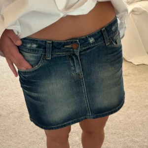 Mörkblå jeanskjol - Säljer en klassisk mörkblå jeanskjol med fem fickor och bälteshällor. Kjolen har en kort passform och stängs med knapp och dragkedja framtill. Perfekt för dig som gillar en enkel och tidlös stil.